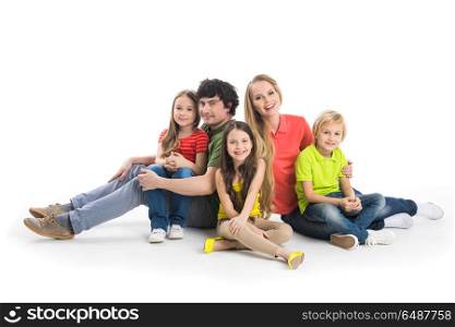 Family with three children. Happy smiling family of two parents and three children sitting on the floor studio isolated on white background