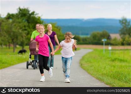 Family with three children (one baby lying in a baby buggy) walking down a path outdoors, two kids are running ahead, there is also a dog
