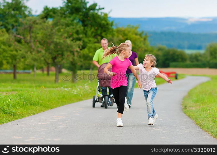 Family with three children (one baby lying in a baby buggy) walking down a path outdoors, the two older daughters running ahead