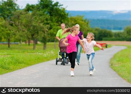 Family with three children (one baby lying in a baby buggy) walking down a path outdoors, the two older daughters running ahead