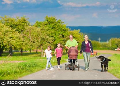 Family with three children (one baby lying in a baby buggy) walking down a path outdoors, there is also a dog
