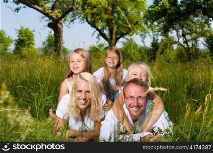 Family with three girls lying in a meadow in summer; they are looking happy
