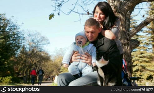 family with toddler looking at the cat on a bench in autumn park