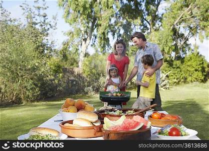 Family with two children (5-6) grilling, table in foreground