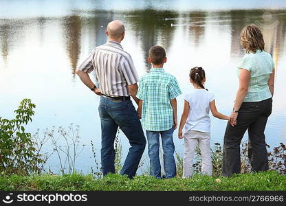 family with two children in early fall park near pond. they are looking at water.