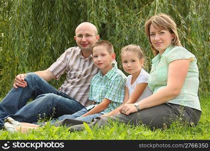 family with two children is sitting at the grass in early fall park