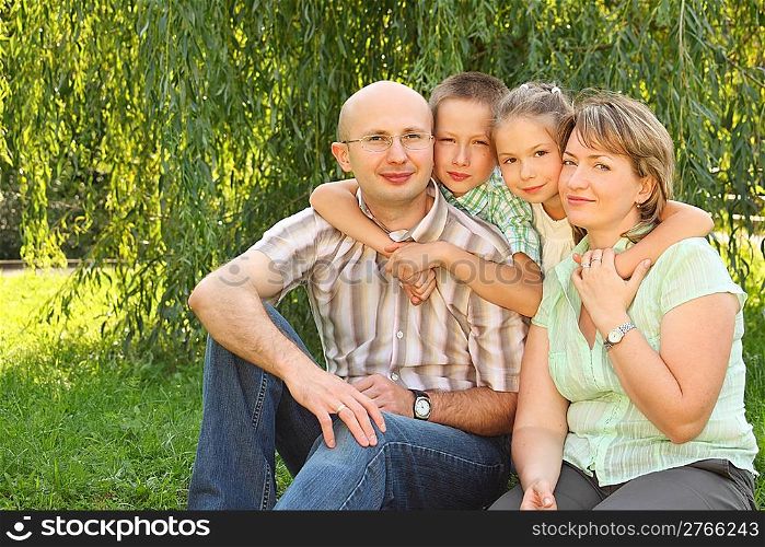 family with two children sitting at the grass near osier and looking at camera