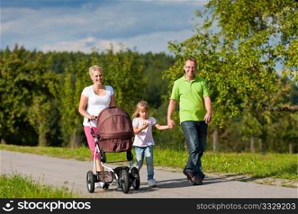 Family with two children (the baby lying in a baby buggy) walking down a path outdoors