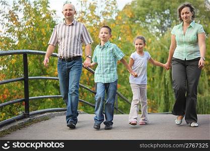 family with two children walking on bridge in early fall park. family is handies. focus on little boy