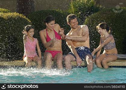Family with two girls splashing, at edge of swimming pool