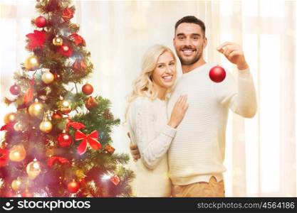 family, x-mas, winter holidays and people concept - happy couple decorating christmas tree with ball at home over lights