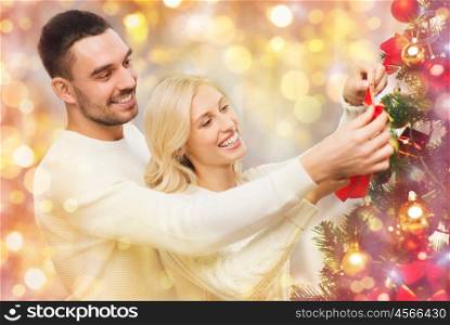 family, x-mas, winter holidays and people concept - happy couple decorating christmas tree with ball at home over lights
