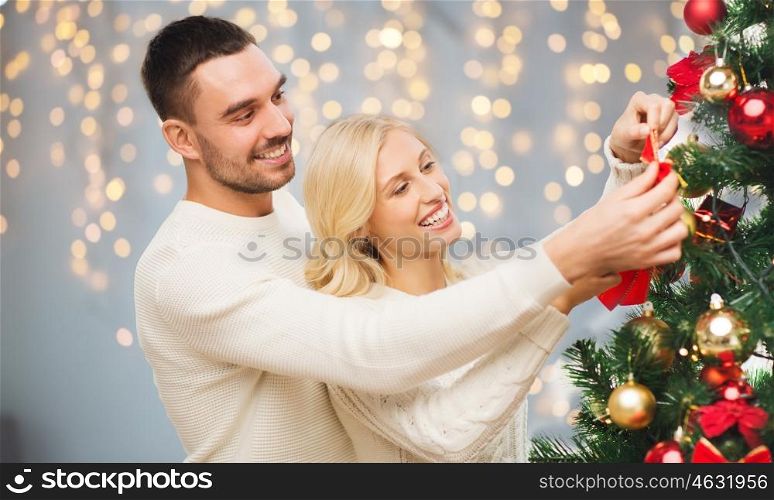 family, x-mas, winter holidays and people concept - happy couple decorating christmas tree over lights background