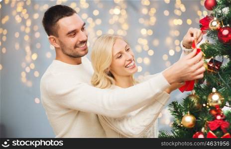 family, x-mas, winter holidays and people concept - happy couple decorating christmas tree over lights background
