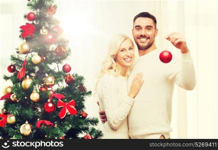 family, x-mas, winter holidays and people concept - happy couple decorating christmas tree with ball at home. happy couple decorating christmas tree at home