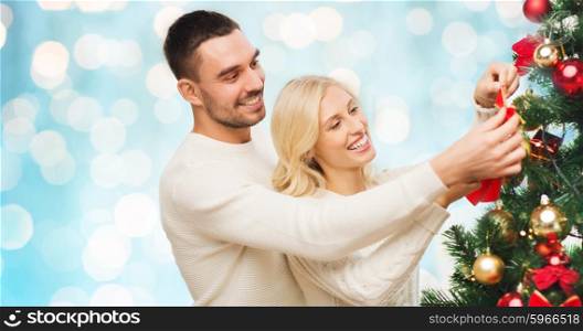 family, x-mas, winter holidays and people concept - happy couple decorating christmas tree at home over blue lights background