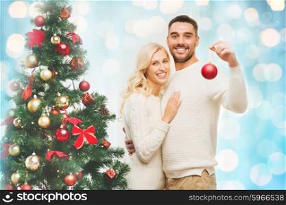 family, x-mas, winter holidays and people concept - happy couple decorating christmas tree with ball at home over blue lights background