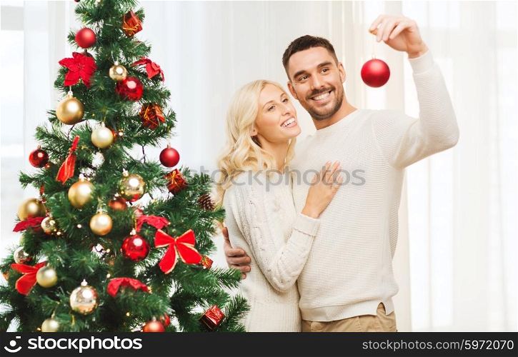 family, x-mas, winter holidays and people concept - happy couple decorating christmas tree with ball at home