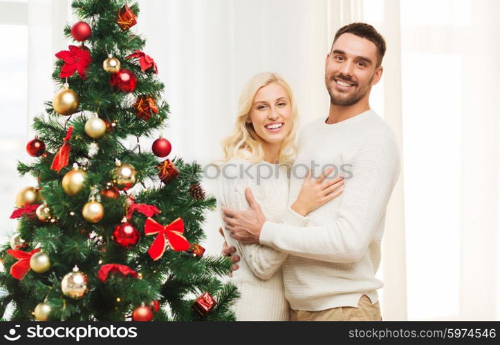 family, x-mas, winter holidays and people concept - happy couple hugging near christmas tree at home