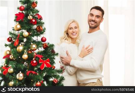 family, x-mas, winter holidays and people concept - happy couple hugging near christmas tree at home