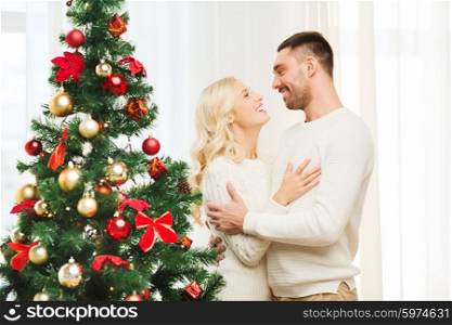 family, x-mas, winter holidays and people concept - happy couple hugging near christmas tree at home