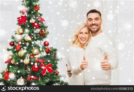 family, x-mas, winter holidays and people concept - happy couple showing thumbs up with christmas tree at home