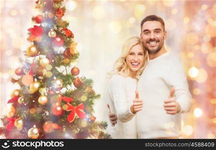 family, x-mas, winter holidays and people concept - happy couple showing thumbs up with christmas tree at home over lights