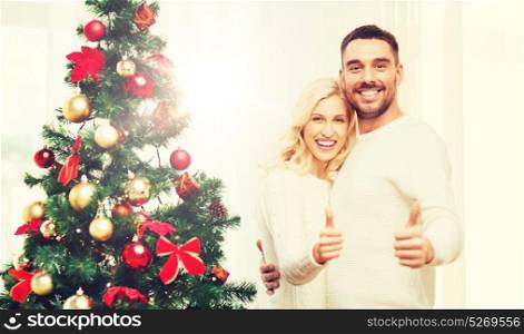 family, x-mas, winter holidays and people concept - happy couple showing thumbs up with christmas tree at home. happy couple showing thumbs up with christmas tree