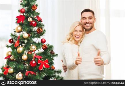 family, x-mas, winter holidays and people concept - happy couple showing thumbs up with christmas tree at home