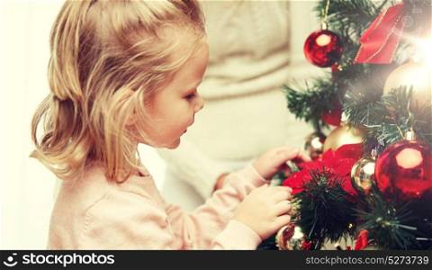 family, x-mas, winter holidays and people concept - happy little girl decorating christmas tree with mother at home. little girl decorating christmas tree at home