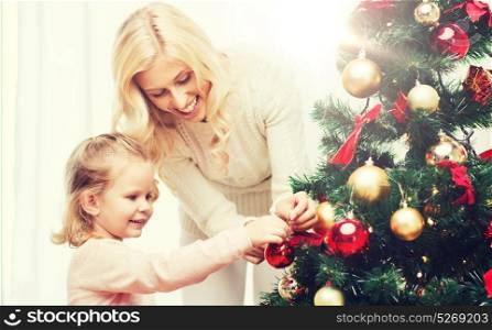 family, x-mas, winter holidays and people concept - happy mother and little daughter decorating christmas tree at home. happy family decorating christmas tree at home