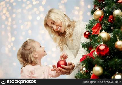 family, x-mas, winter holidays and people concept - happy mother and little daughter decorating christmas tree over lights background. happy family decorating christmas tree