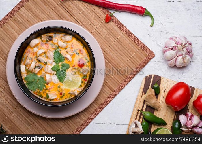 famous delicious Thai Tom yum spicy soup with champignon on bamboo napkin. served on white table with vegetables. flat lay