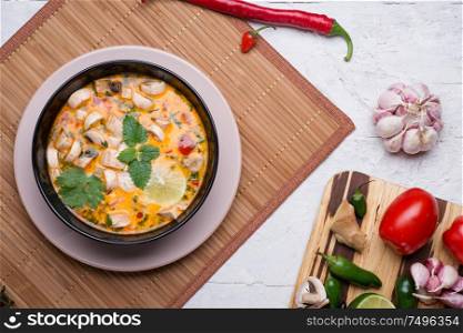 famous delicious Thai Tom yum spicy soup with champignon on bamboo napkin. served on white table with vegetables. flat lay