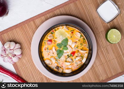 famous delicious Thai Tom yum spicy soup with champignon on bamboo napkin. served on white table. flat lay