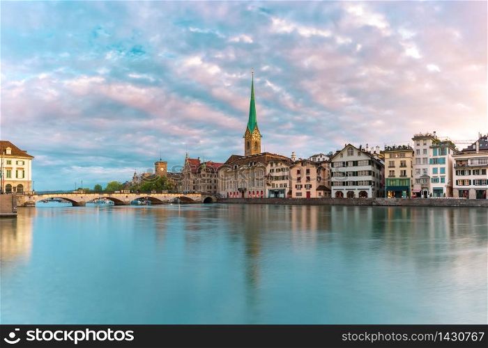 Famous Fraumunster church with its reflection in river Limmat at pink sunrise in Old Town of Zurich, the largest city in Switzerland. Zurich, largest city in Switzerland