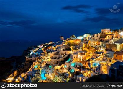 Famous greek iconic picturesque tourist destination Oia village with traditional white houses and windmills in Santorini island in the evening blue hour, Greece. Famous greek tourist destination Oia, Greece