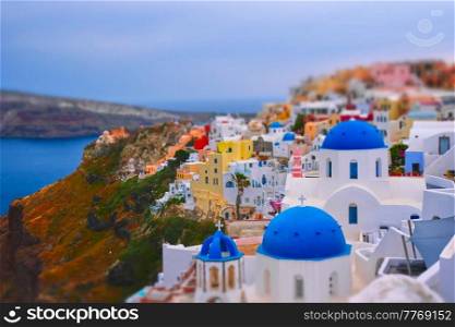Famous greek iconic selfie spot tourist destination Oia village with traditional white houses and church in Santorini island on sunset in twilight, Greece. Toy camera tilt shift miniature effect. Famous greek tourist destination Oia, Greece
