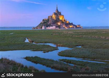 Famous Mont Saint Michel Illuminated in the evening blue hour with reflection in the canal on the water meadows, Normandy, France. Night Mont Saint Michel, Normandy, France