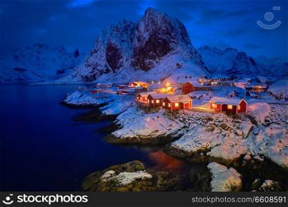 Famous tourist attraction Hamnoy fishing village on Lofoten Islands, Norway with red rorbu houses in winter snow illuminated in the evening. Hamnoy fishing village on Lofoten Islands, Norway 