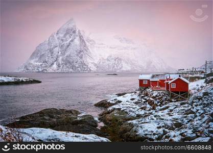 Famous tourist attraction Hamnoy fishing village on Lofoten Islands, Norway with red rorbu houses. With falling snow in winter on sunrise. Hamnoy fishing village on Lofoten Islands, Norway 
