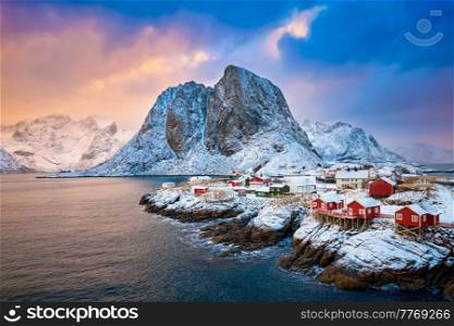 Famous tourist attraction Hamnoy fishing village on Lofoten Islands, Norway with red rorbu houses. With falling snow in winter on sunrise. Hamnoy fishing village on Lofoten Islands, Norway