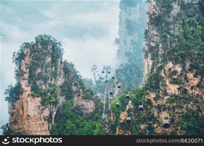 Famous tourist attraction of China - Zhangjiajie stone pillars cliff mountains in fog clouds with cable railway car lift at Wulingyuan, Hunan, China. With camera pan. Zhangjiajie mountains, China