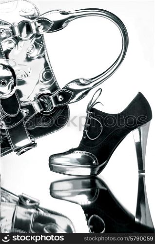 Fancy black and silver shoe with a silver bag on a reflective mirror surface in high contrast.