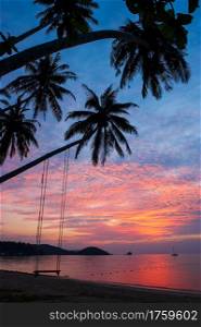 Fantastic clouds and sunset sky over the tropical island, beautiful shape of coconut palm trees and swing on the beach, serene scene on summer dusk. Koh Mak Island, Thailand.