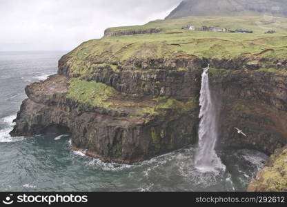 Fantastic landscape view to the worth the visit village of Gasadalur and one of the most surreal waterfalls Mulafossur on the Vagar Island of the Faroe Islands. Landscape with waterfall and rocks. Glorious sceneries of the Faroes. Postcard motif.