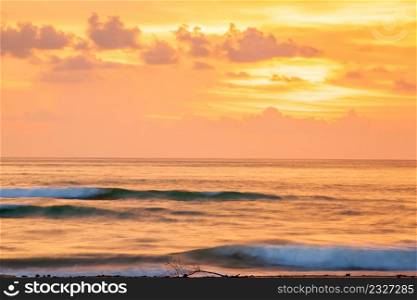 Fantastic scenic seascape at dusk, colorful sunset sky with clouds in summertime. A soft orange glow blankets the sky as gently waves. Long exposure. Motion blurred backgrounds and surface.