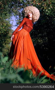 Fantasy. Artistic Stylized Woman in Trendy Red Dress and Big Frizzy Wig