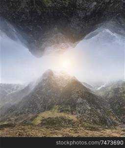 Fantasy composite image of inverted mountain landscape above norma lmountain landscape with sun burst in sky inbetween