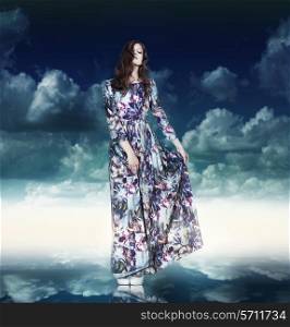 Fantasy. Luxurious Woman in Variegated Dress over Blue Sky